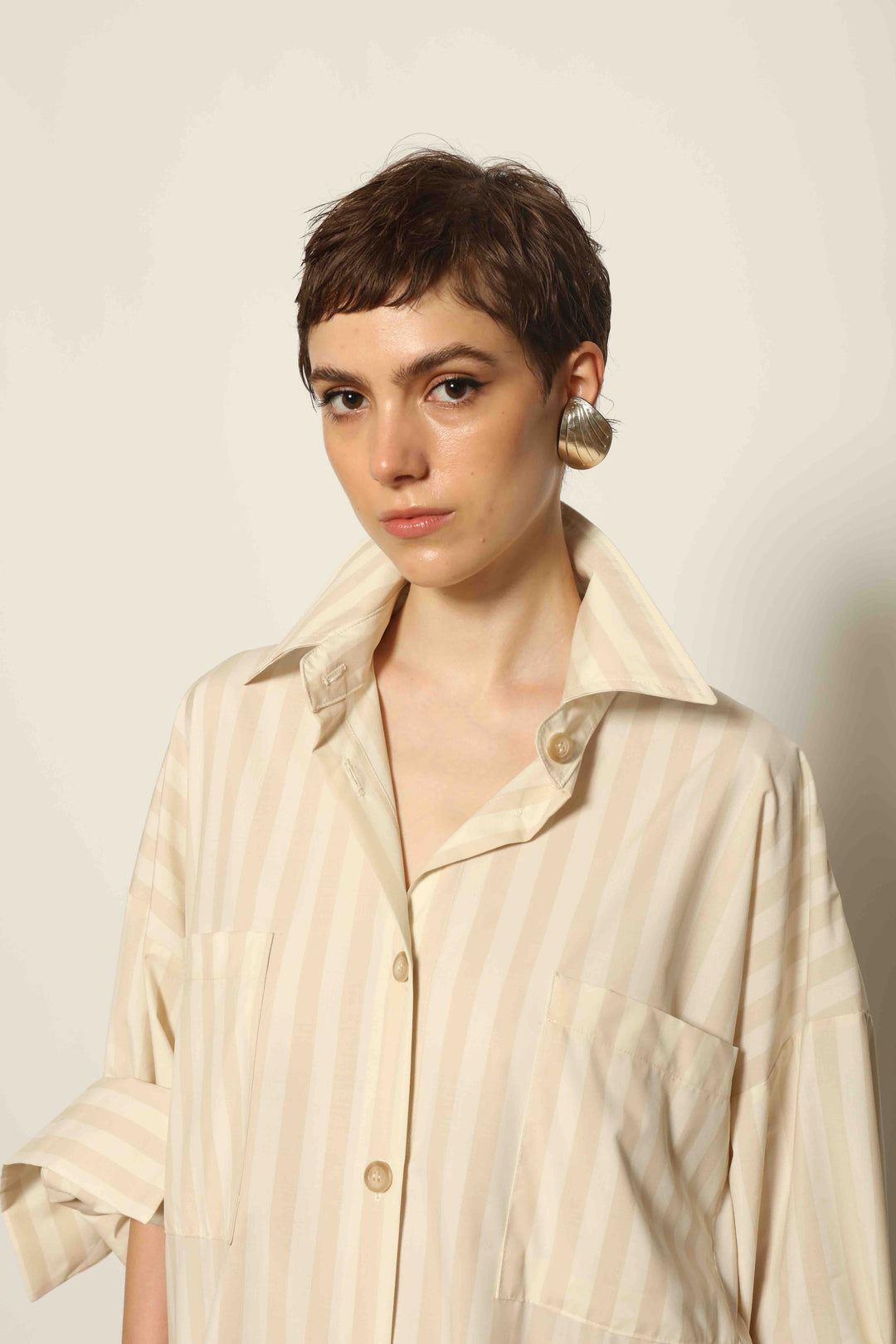 Model is wearing the Sand White Striped Bettina Dress by House of Nomad Stories, featuring a fluid silhouette with subtle sand and white vertical stripes and a soft, elegant drape.