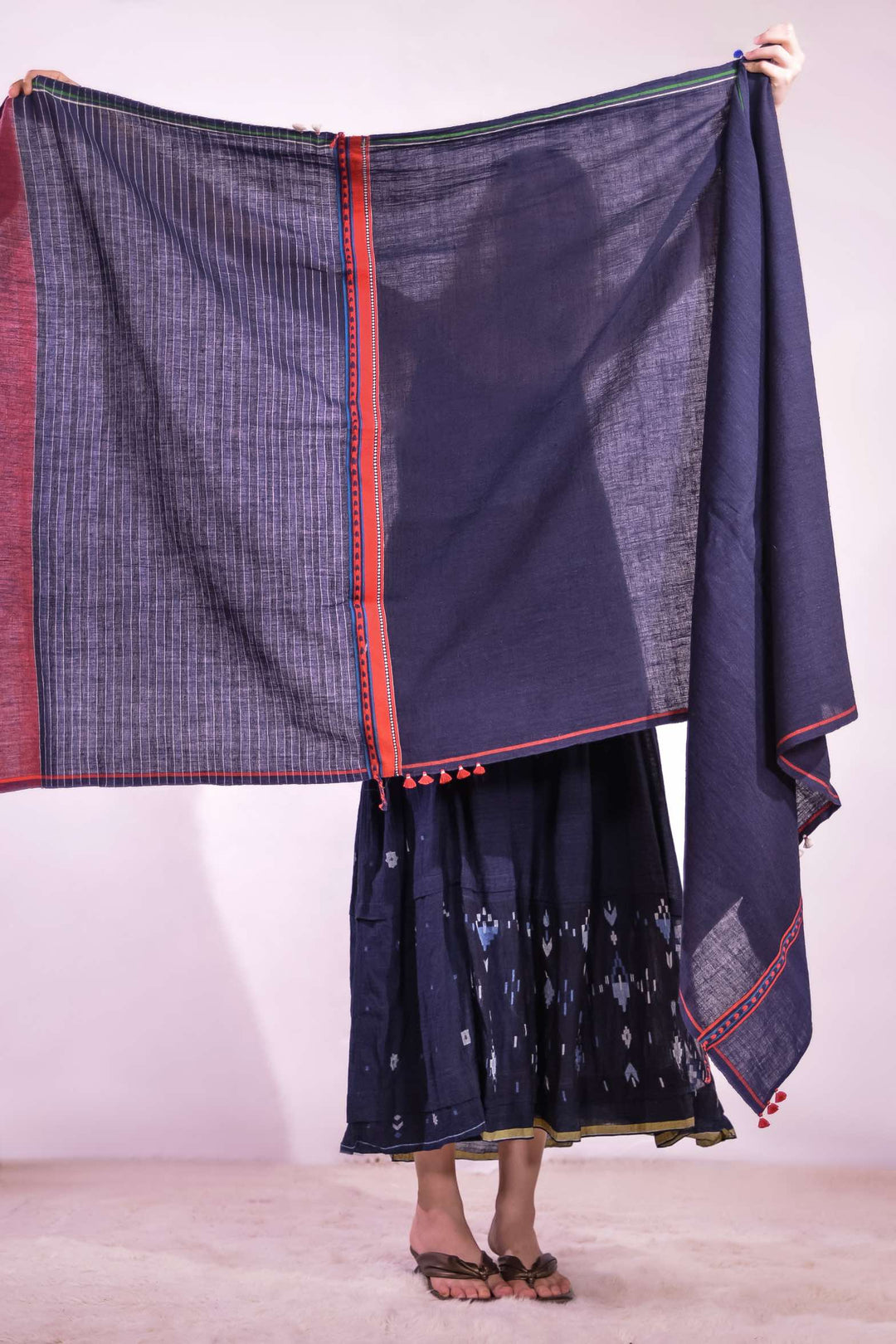 Model wearing pure cotton scarf by Injiri – handloomed unisex accessory in natural indigo with red and white woven details, crafted from organic cotton and finished with tassels. Ethically handmade in India.