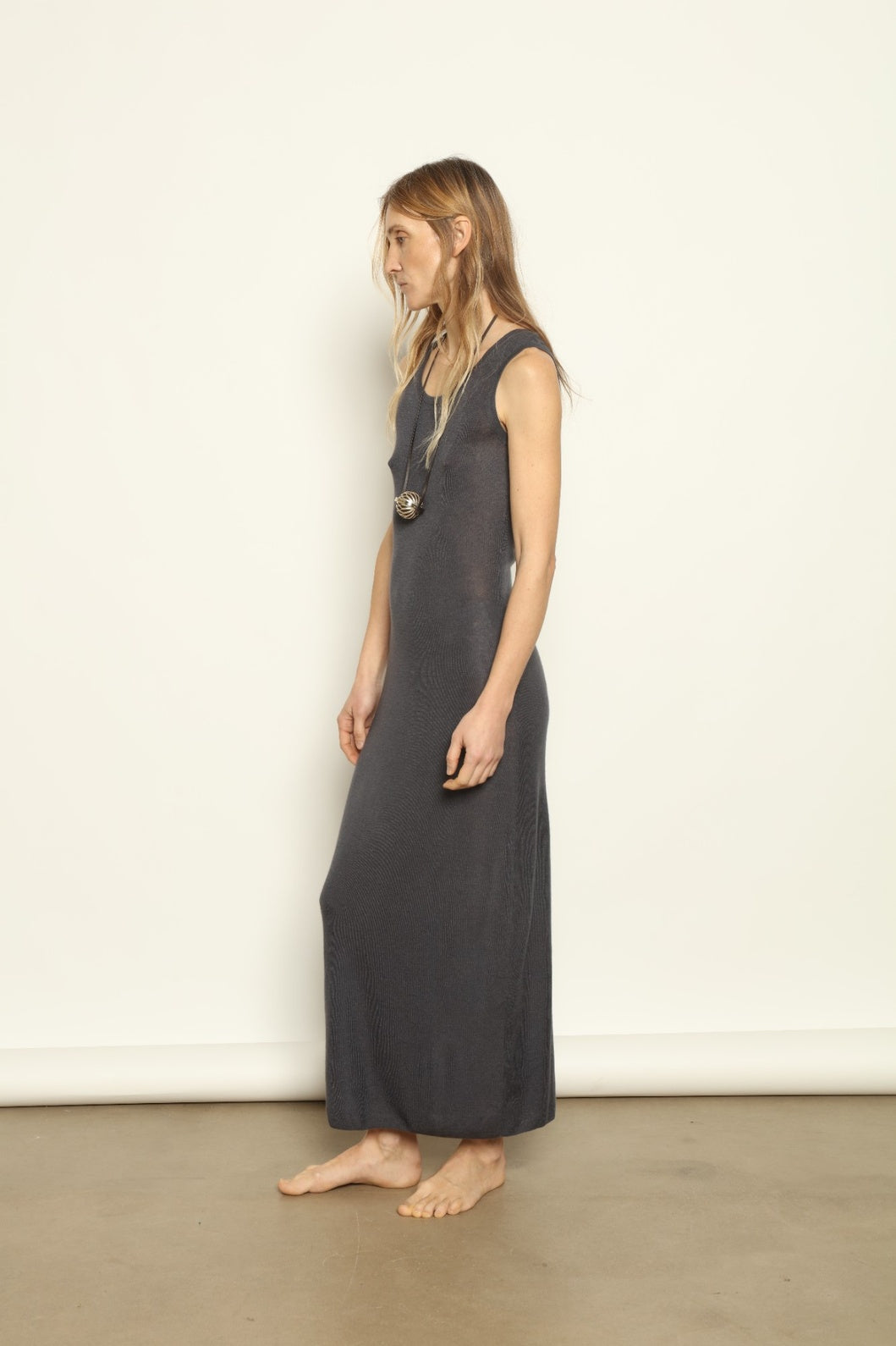 Deep indigo cashmere dress by Mirror in the Sky with an elongated, fluid silhouette. Woman wearing a long dark dress against a plain background