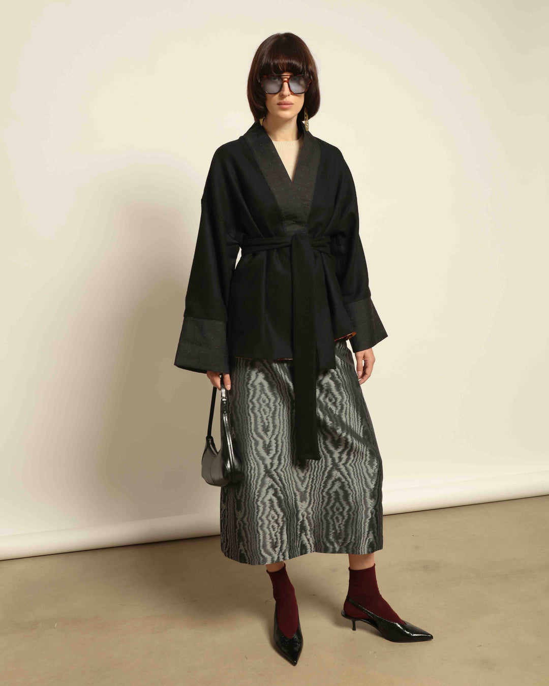 Lunatica Milano grey skirt from House of Nomad Stories crafted from lightweight moiré fabric. The model is wearing the Obidi Midnight Kantha Jacket in pure black, made of wool with a silk collar and Kantha silk lining, a timeless and versatile piece.