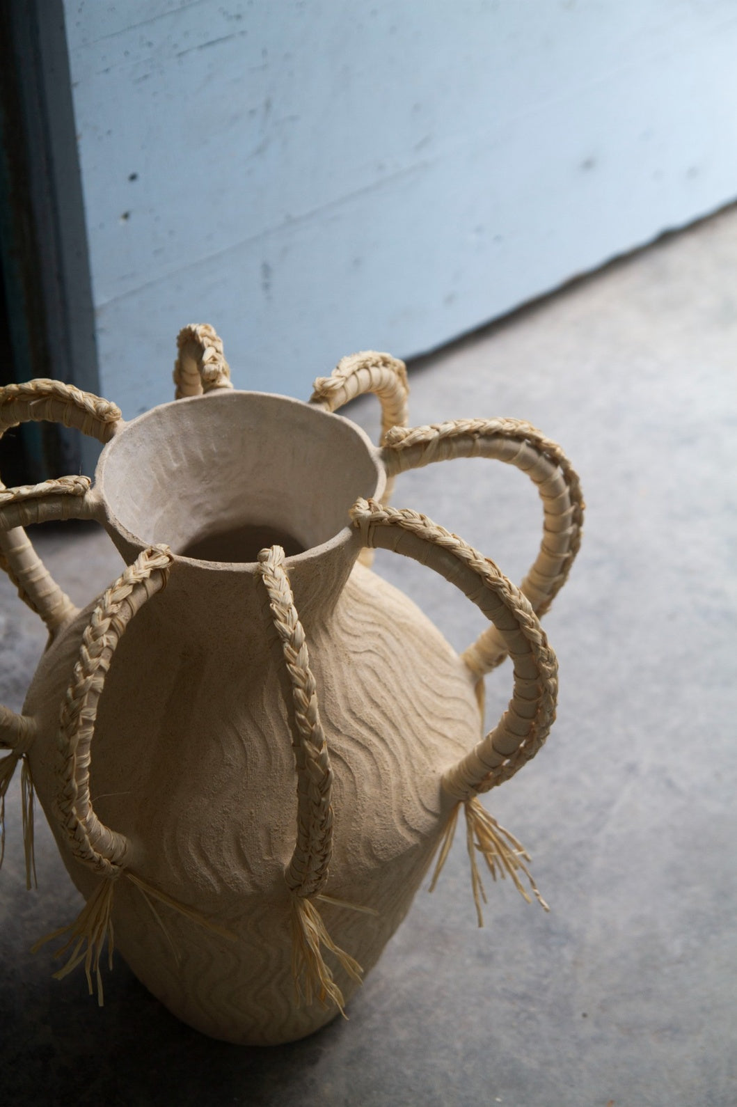 Amphora Ondas by Clandestine Céramique, handbuilt in sandy clay with engraved wave patterns and eight braided raphia handles, part of the House of Nomad Stories selection.