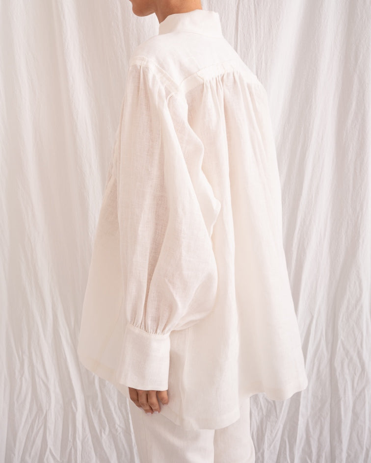 Model is wearing the Ancestral White Linen Shirt by Les Vacances d’Irina, a unisex handmade linen shirt with relaxed cut, open V-neckline, and natural shell buttons, crafted in Bucharest and available at House of Nomad Stories.