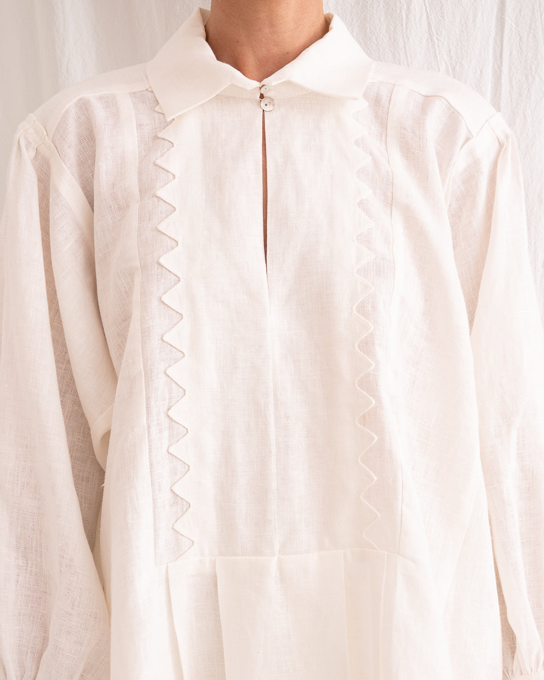 Model is wearing the Ancestral White Linen Shirt by Les Vacances d’Irina, a unisex handmade linen shirt with relaxed cut, open V-neckline, and natural shell buttons, crafted in Bucharest and available at House of Nomad Stories.