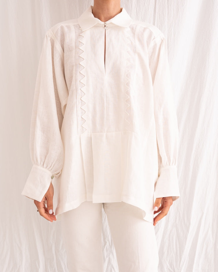 Model is wearing the Ancestral White Linen Shirt by Les Vacances d’Irina, a unisex handmade linen shirt with relaxed cut, open V-neckline, and natural shell buttons, crafted in Bucharest and available at House of Nomad Stories.