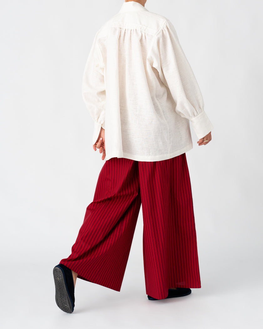 Model is wearing the Ancestral White Linen Shirt by Les Vacances d’Irina, a unisex handmade linen shirt with relaxed cut, open V-neckline, and natural shell buttons, crafted in Bucharest and available at House of Nomad Stories.