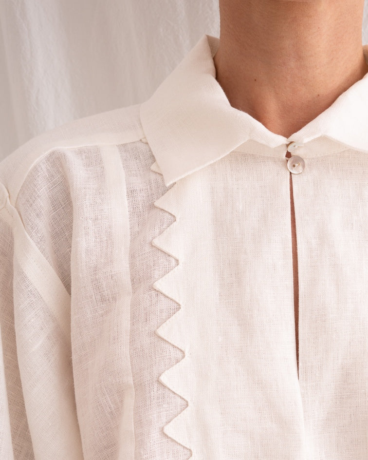 Model is wearing the Ancestral White Linen Shirt by Les Vacances d’Irina, a unisex handmade linen shirt with relaxed cut, open V-neckline, and natural shell buttons, crafted in Bucharest and available at House of Nomad Stories.