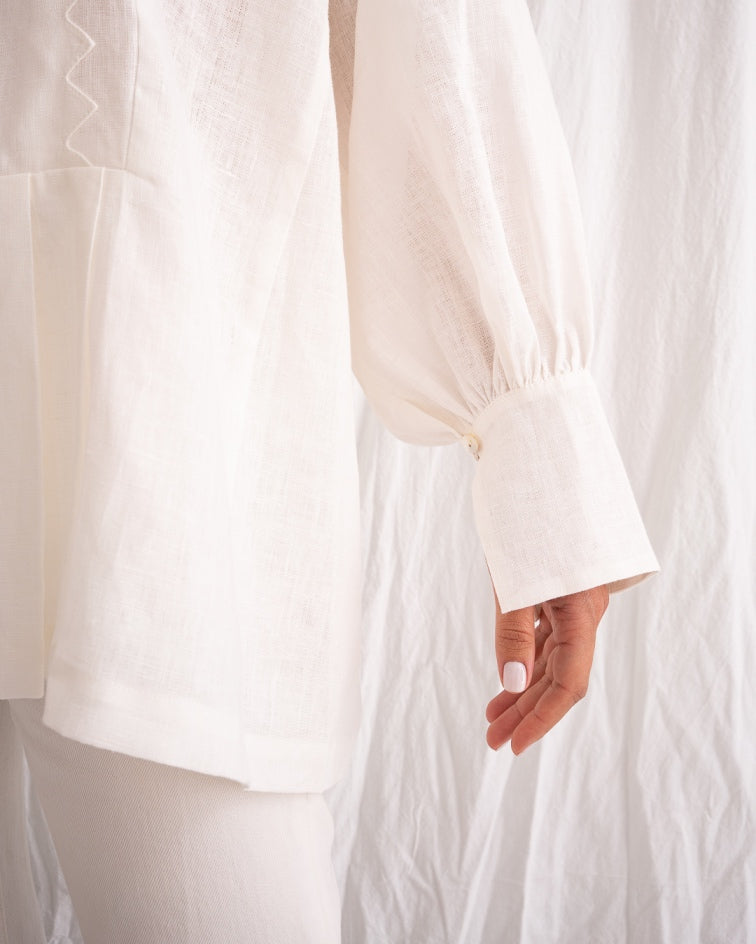 Model is wearing the Ancestral White Linen Shirt by Les Vacances d’Irina, a unisex handmade linen shirt with relaxed cut, open V-neckline, and natural shell buttons, crafted in Bucharest and available at House of Nomad Stories.