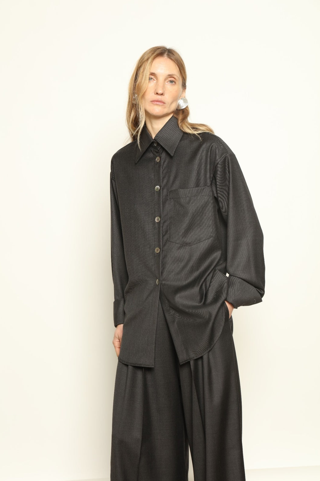 Model is wearing the Anthracite Oscar Shirt by House of Nomad Stories, crafted from 100% Super 100 Pure Merino Cool Wool with a clean minimalist silhouette, sharp collar, and long sleeves.