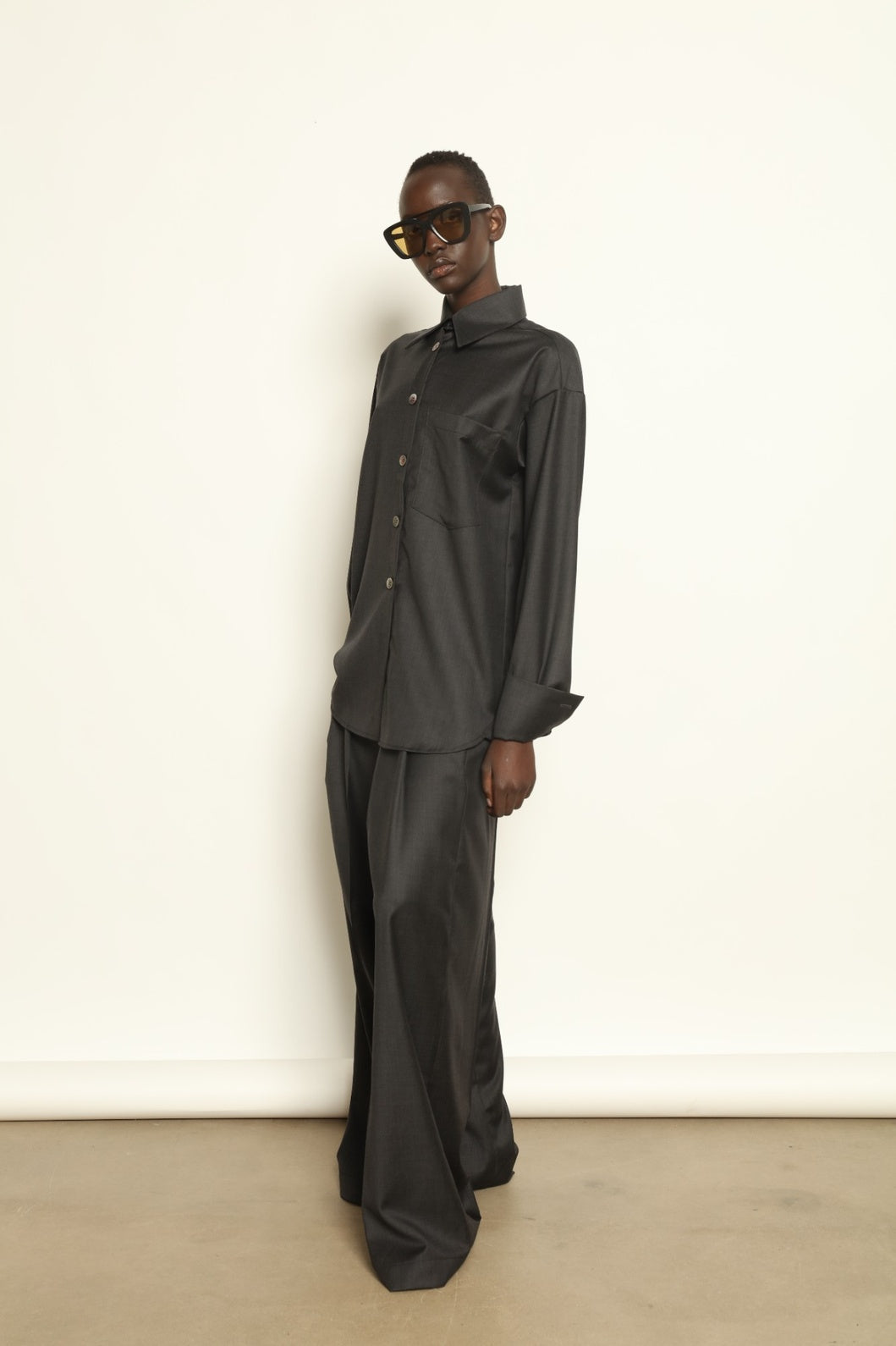 Model is wearing the Anthracite Oscar Shirt by House of Nomad Stories, crafted from 100% Super 100 Pure Merino Cool Wool with a clean minimalist silhouette, sharp collar, and long sleeves.