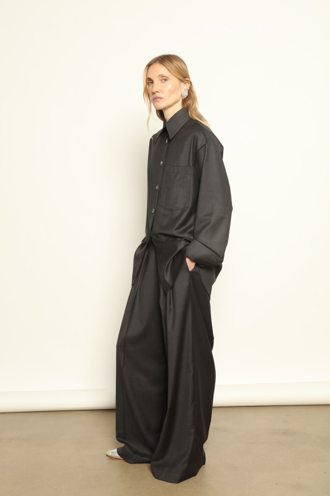 Model is wearing the Anthracite Oscar Shirt by House of Nomad Stories, crafted from 100% Super 100 Pure Merino Cool Wool with a clean minimalist silhouette, sharp collar, and long sleeves.