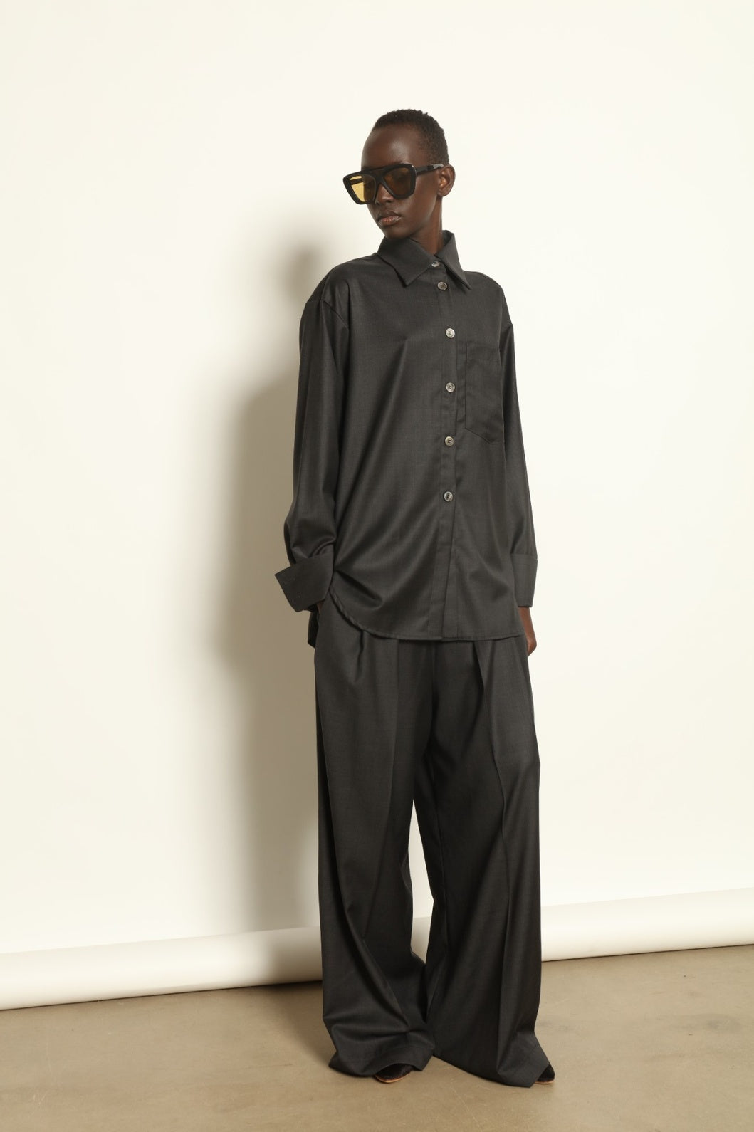 Model is wearing the Anthracite Oscar Shirt by House of Nomad Stories, crafted from 100% Super 100 Pure Merino Cool Wool with a clean minimalist silhouette, sharp collar, and long sleeves.