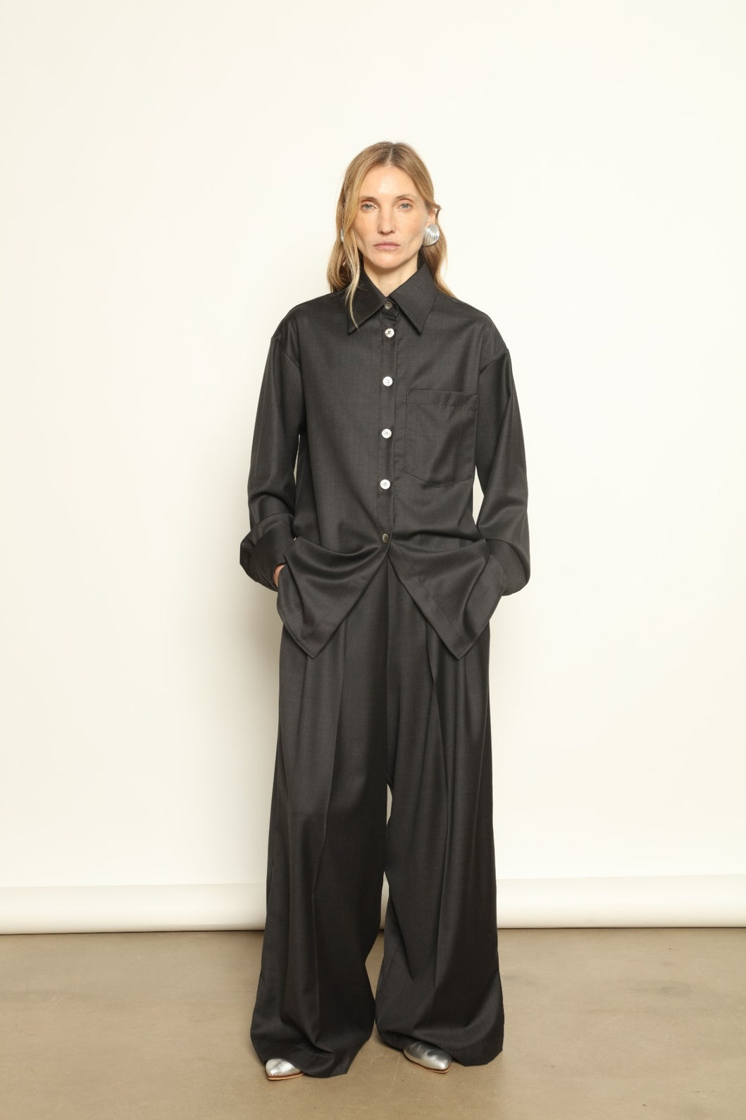 Model is wearing the Anthracite Oscar Shirt by House of Nomad Stories, crafted from 100% Super 100 Pure Merino Cool Wool with a clean minimalist silhouette, sharp collar, and long sleeves.