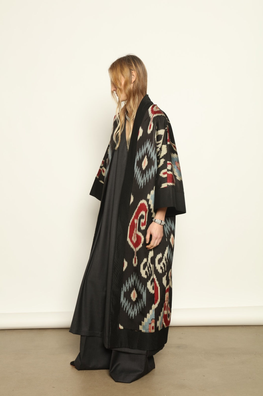 Model is wearing the Aura XL Ikat Silk Coat by Aleksandra Viktor, part of House of Nomad Stories collection, handwoven Uzbek ikat silk coat with XL silhouette, expressive ikat motifs, and deep red lining