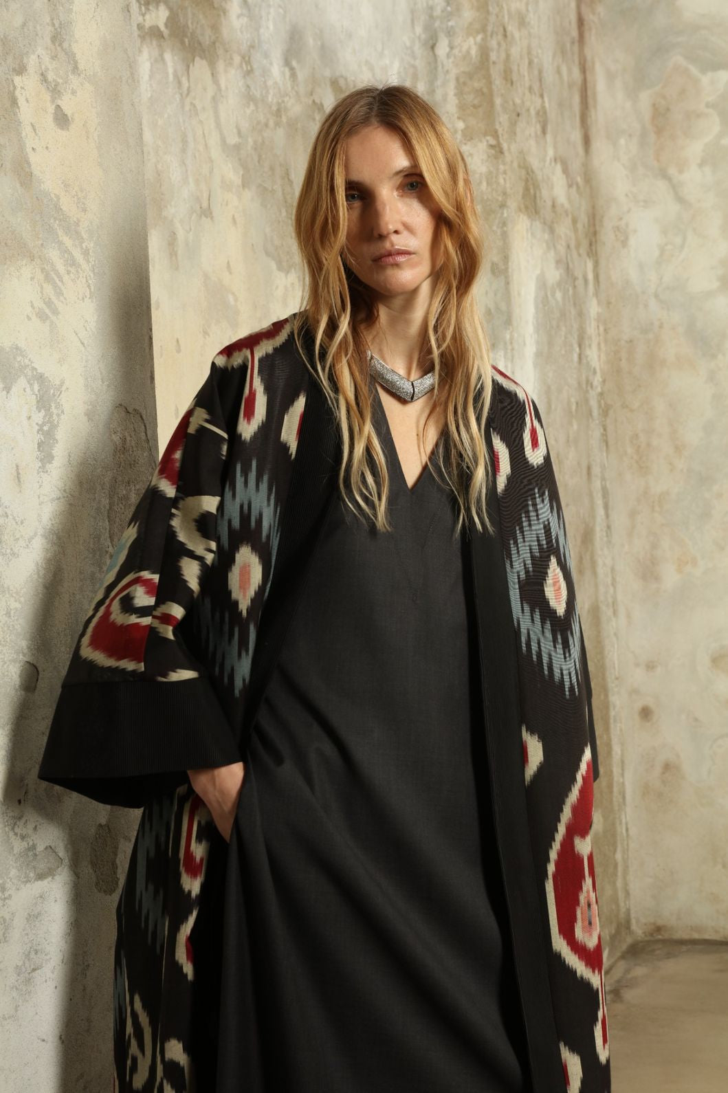 Model is wearing the Aura XL Ikat Silk Coat by Aleksandra Viktor, part of House of Nomad Stories collection, handwoven Uzbek ikat silk coat with XL silhouette, expressive ikat motifs, and deep red lining