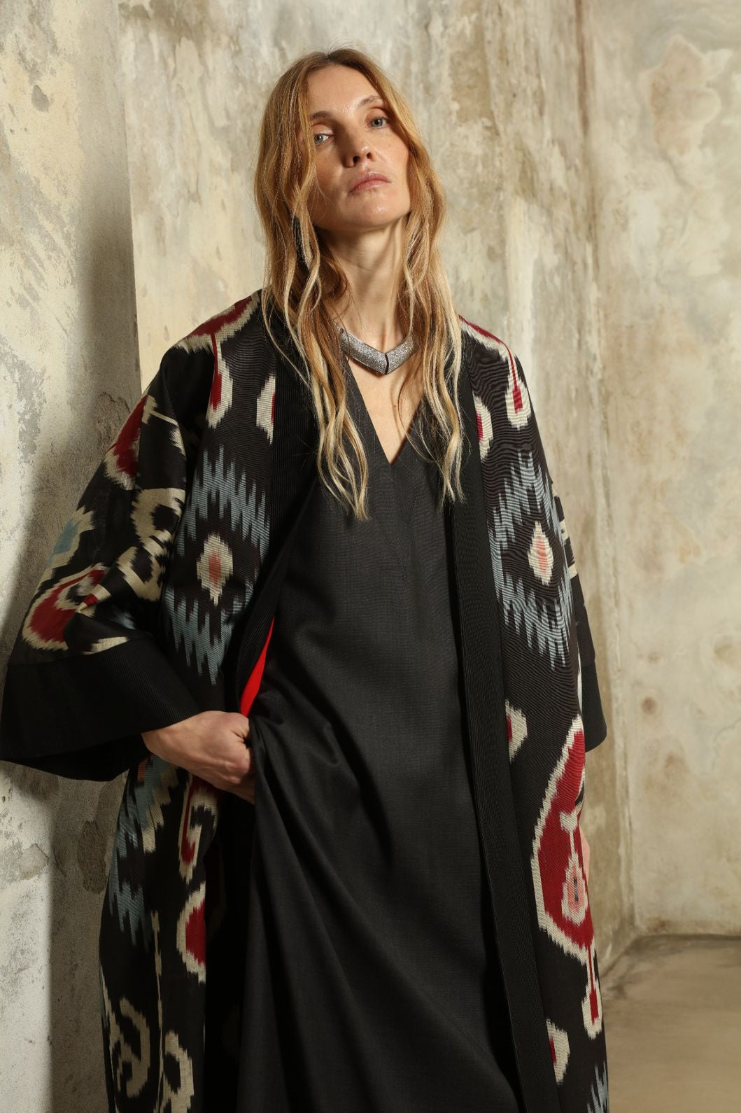 Model is wearing the Aura XL Ikat Silk Coat by Aleksandra Viktor, part of House of Nomad Stories collection, handwoven Uzbek ikat silk coat with XL silhouette, expressive ikat motifs, and deep red lining