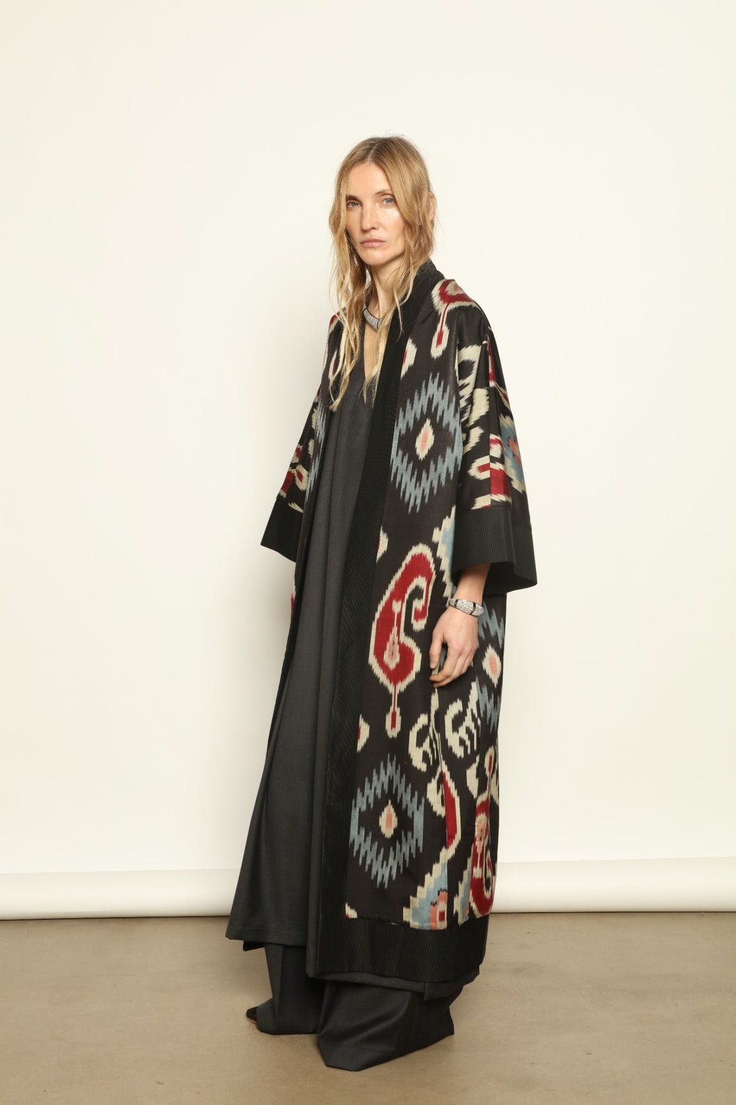 Model is wearing the Aura XL Ikat Silk Coat by Aleksandra Viktor, part of House of Nomad Stories collection, handwoven Uzbek ikat silk coat with XL silhouette, expressive ikat motifs, and deep red lining
