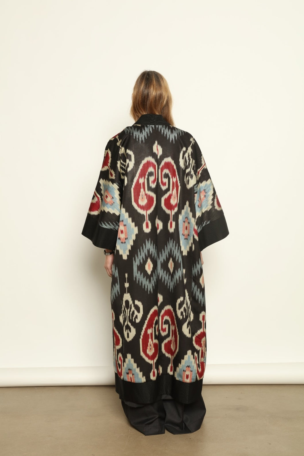 Model is wearing the Aura XL Ikat Silk Coat by Aleksandra Viktor, part of House of Nomad Stories collection, handwoven Uzbek ikat silk coat with XL silhouette, expressive ikat motifs, and deep red lining