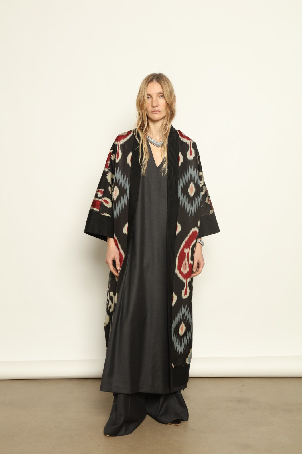 Model is wearing the Aura XL Ikat Silk Coat by Aleksandra Viktor, part of House of Nomad Stories collection, handwoven Uzbek ikat silk coat with XL silhouette, expressive ikat motifs, and deep red lining