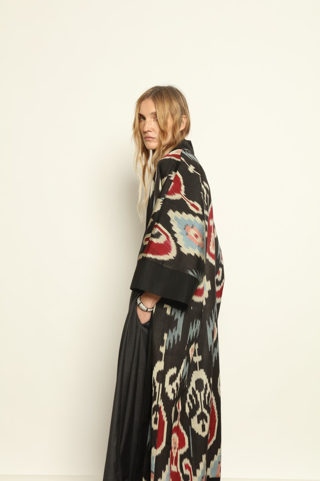 Model is wearing the Aura XL Ikat Silk Coat by Aleksandra Viktor, part of House of Nomad Stories collection, handwoven Uzbek ikat silk coat with XL silhouette, expressive ikat motifs, and deep red lining
