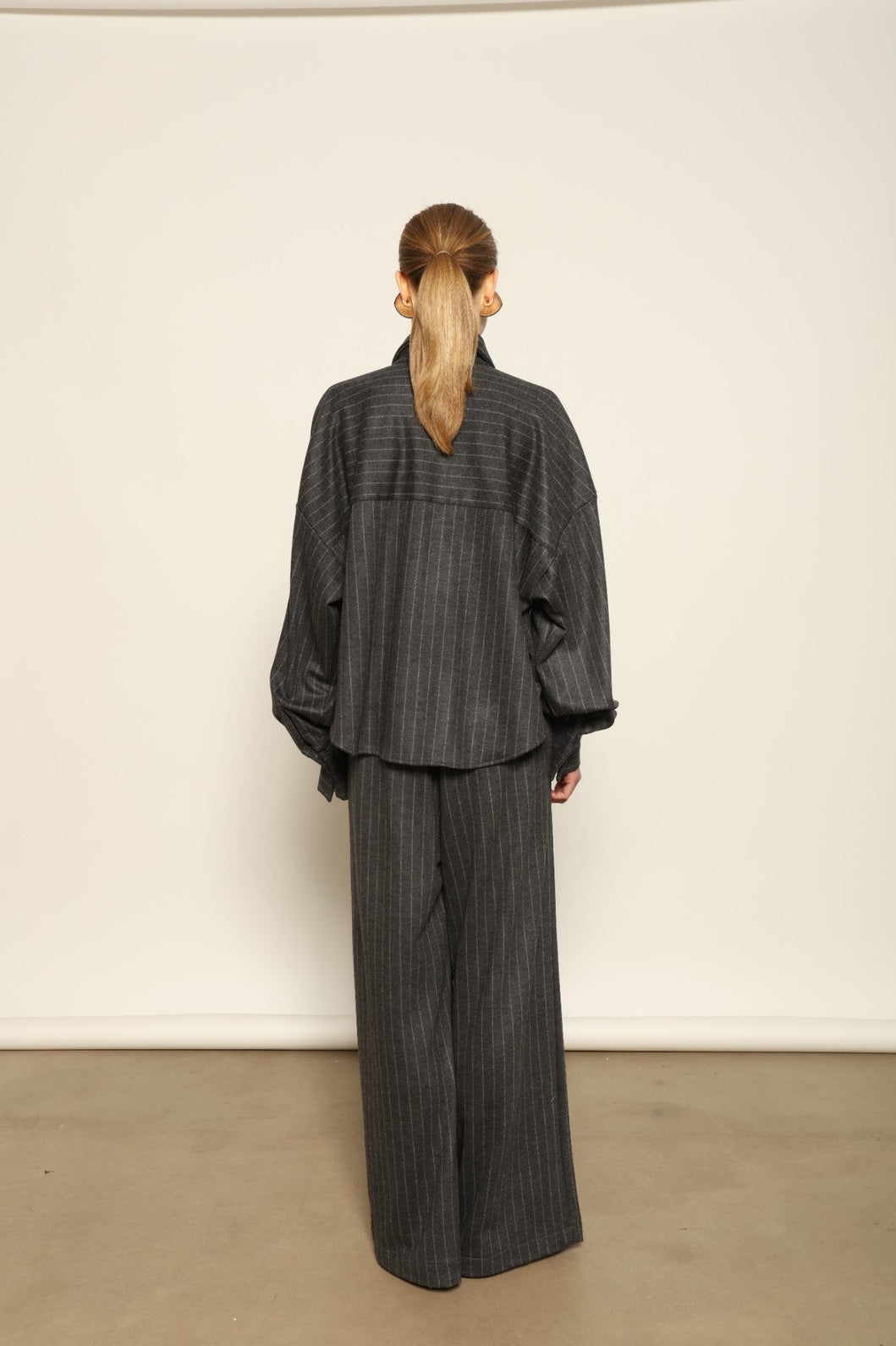 Model is wearing Bettina Striped Grey and White Double Jersey Shirt by House of Nomad Stories, part of the curated selection, handcrafted in Italy from linen, wool, and silk blend with vertical stripes, relaxed tailoring, and fluid drape for timeless elegance.