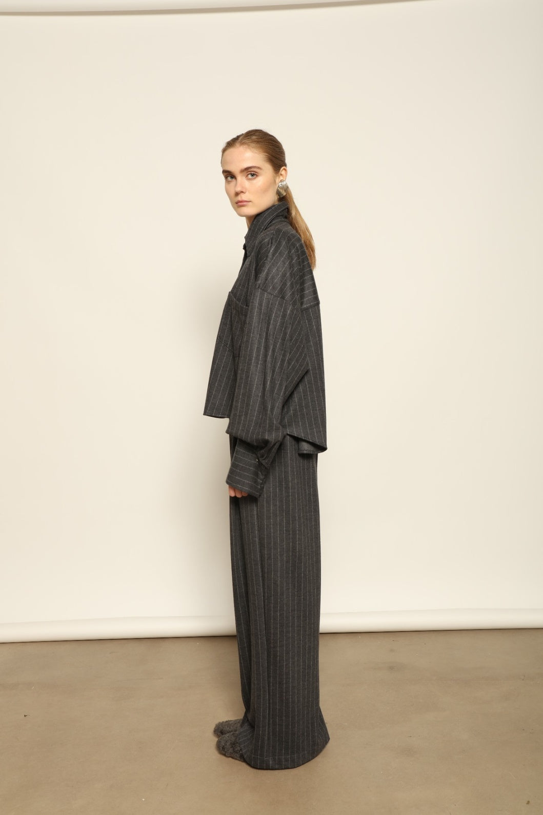 Model is wearing Bettina Striped Grey and White Double Jersey Shirt by House of Nomad Stories, part of the curated selection, handcrafted in Italy from linen, wool, and silk blend with vertical stripes, relaxed tailoring, and fluid drape for timeless elegance.