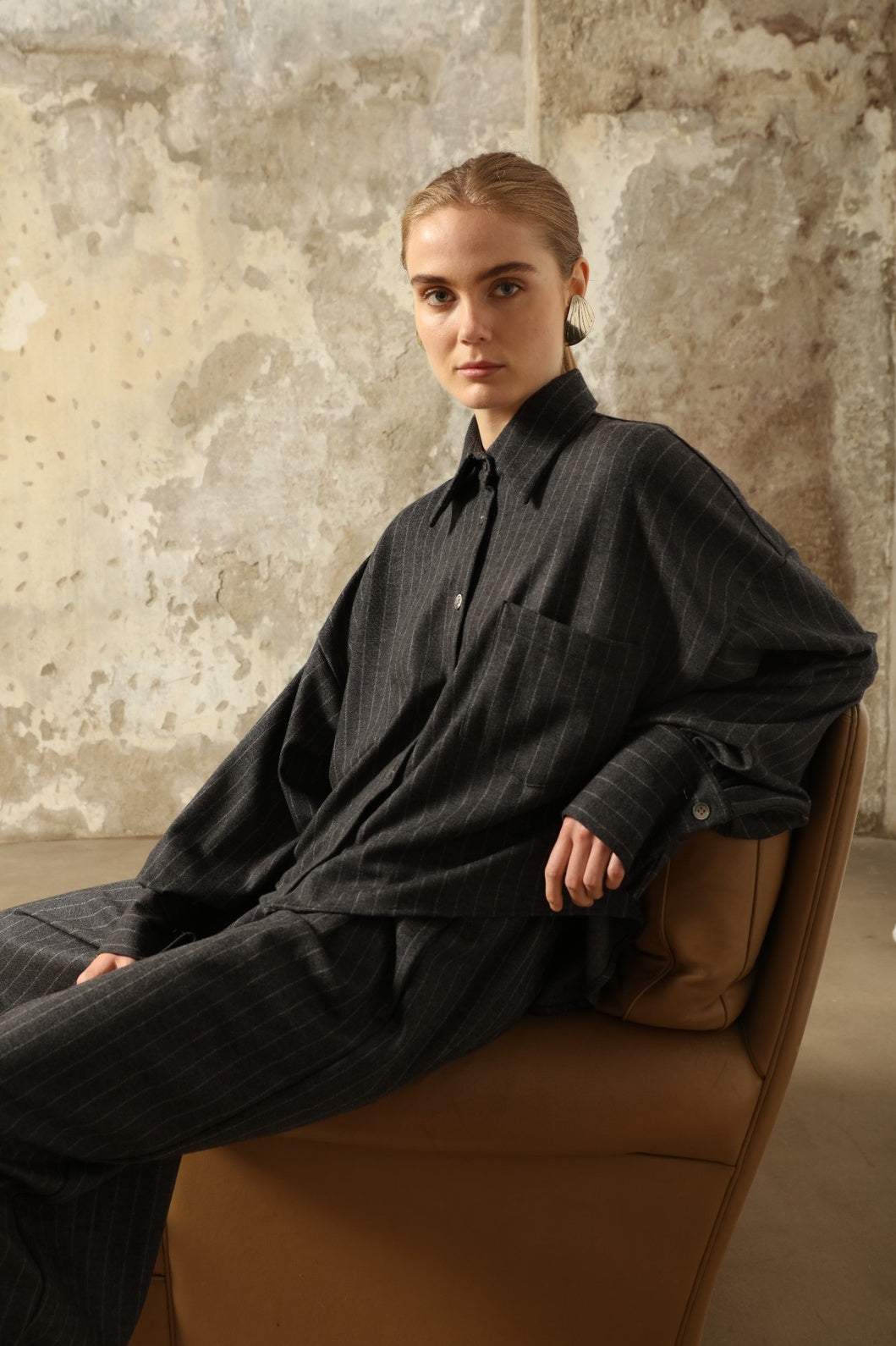Model is wearing Bettina Striped Grey and White Double Jersey Shirt by House of Nomad Stories, part of the curated selection, handcrafted in Italy from linen, wool, and silk blend with vertical stripes, relaxed tailoring, and fluid drape for timeless elegance.
