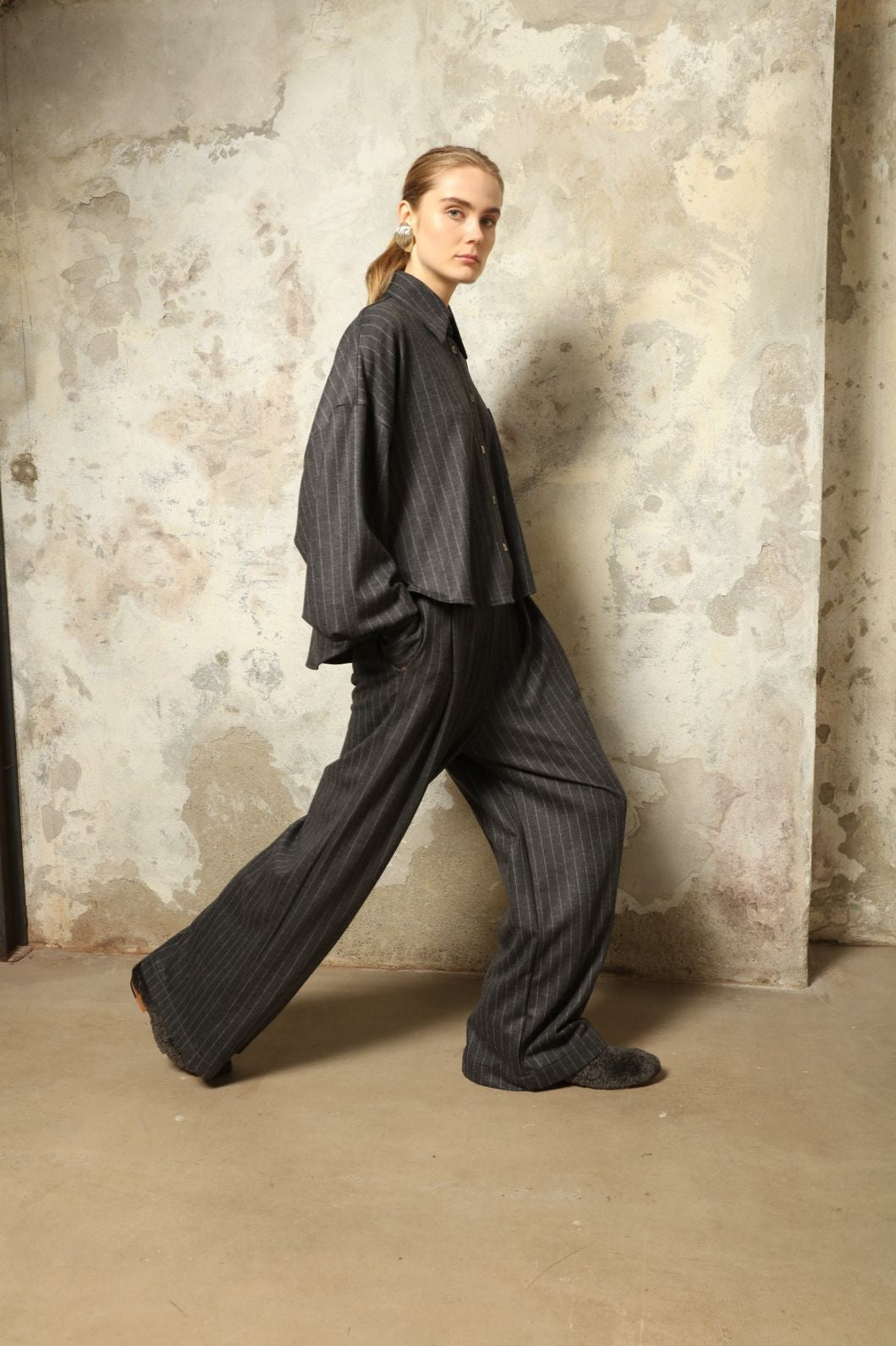 xModel is wearing Bettina Striped Grey and White Double Jersey Shirt by House of Nomad Stories, part of the curated selection, handcrafted in Italy from linen, wool, and silk blend with vertical stripes, relaxed tailoring, and fluid drape for timeless elegance.