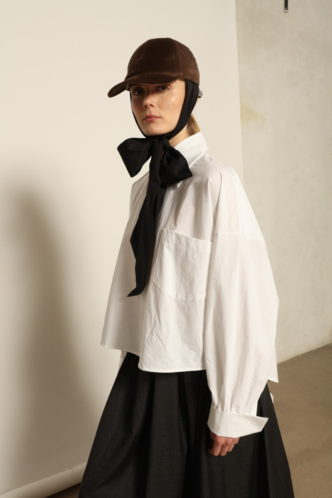 Model is wearing the Bettina White Organic Cotton Blouse by House of Nomad Stories, featuring a straight silhouette, classic collar, button-front closure, and oversized chest pocket.