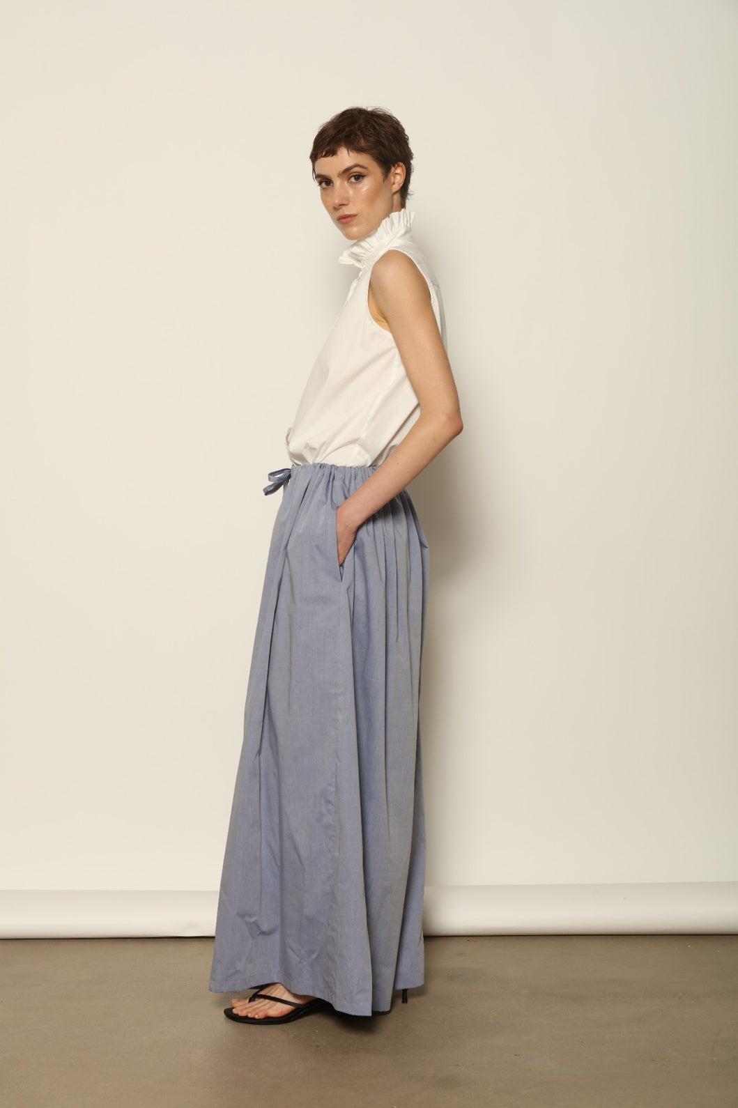 Model is wearing the Brigitta dusty blue cotton mousseline trousers from the House of Nomad Stories selection, lightweight and breathable women’s summer pants made in Italy in Piedmont, crafted from 100% natural cotton with a relaxed tailored silhouette designed for effortless movement.