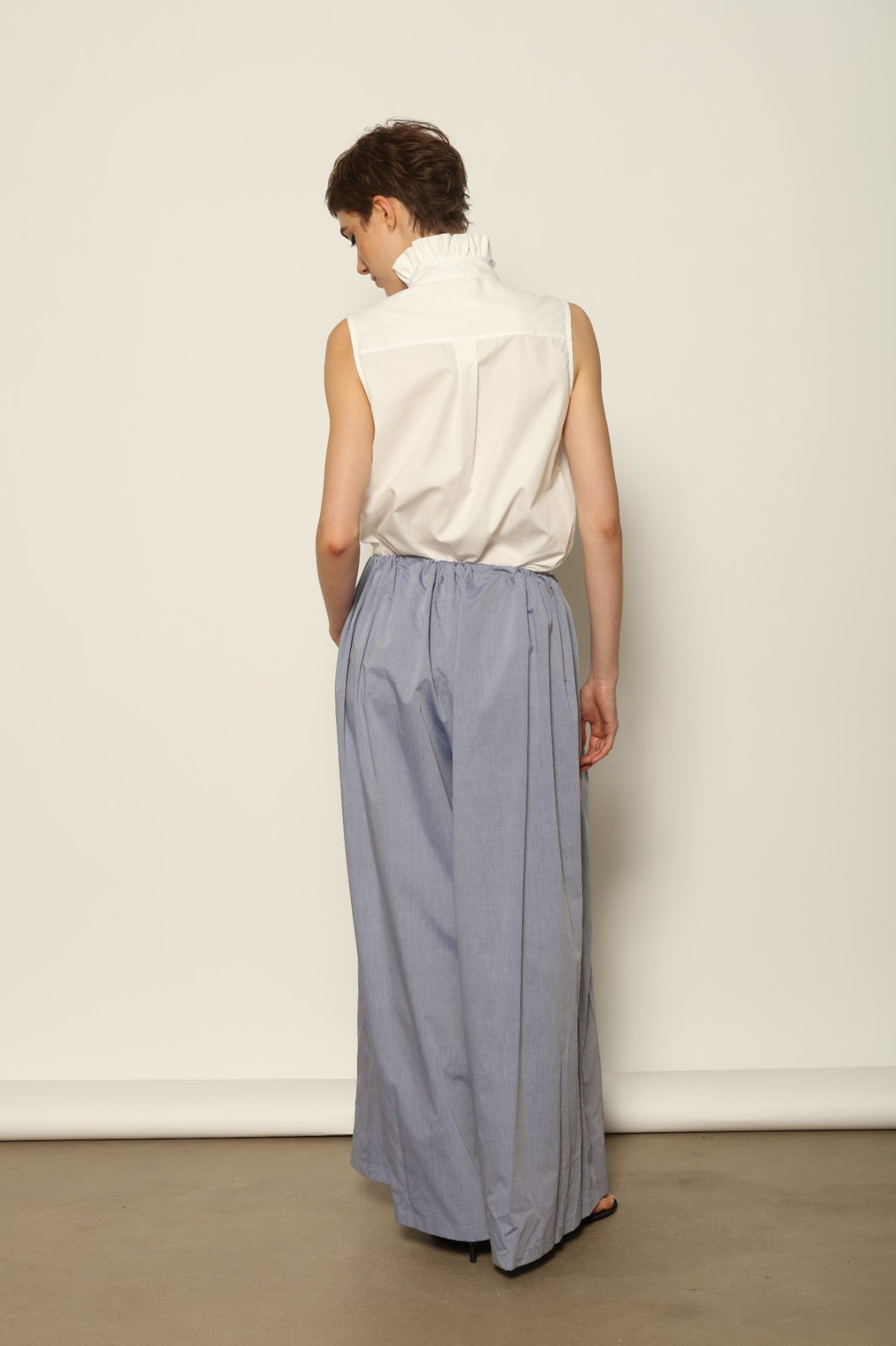 Model is wearing the Brigitta dusty blue cotton mousseline trousers from the House of Nomad Stories selection, lightweight and breathable women’s summer pants made in Italy in Piedmont, crafted from 100% natural cotton with a relaxed tailored silhouette designed for effortless movement.