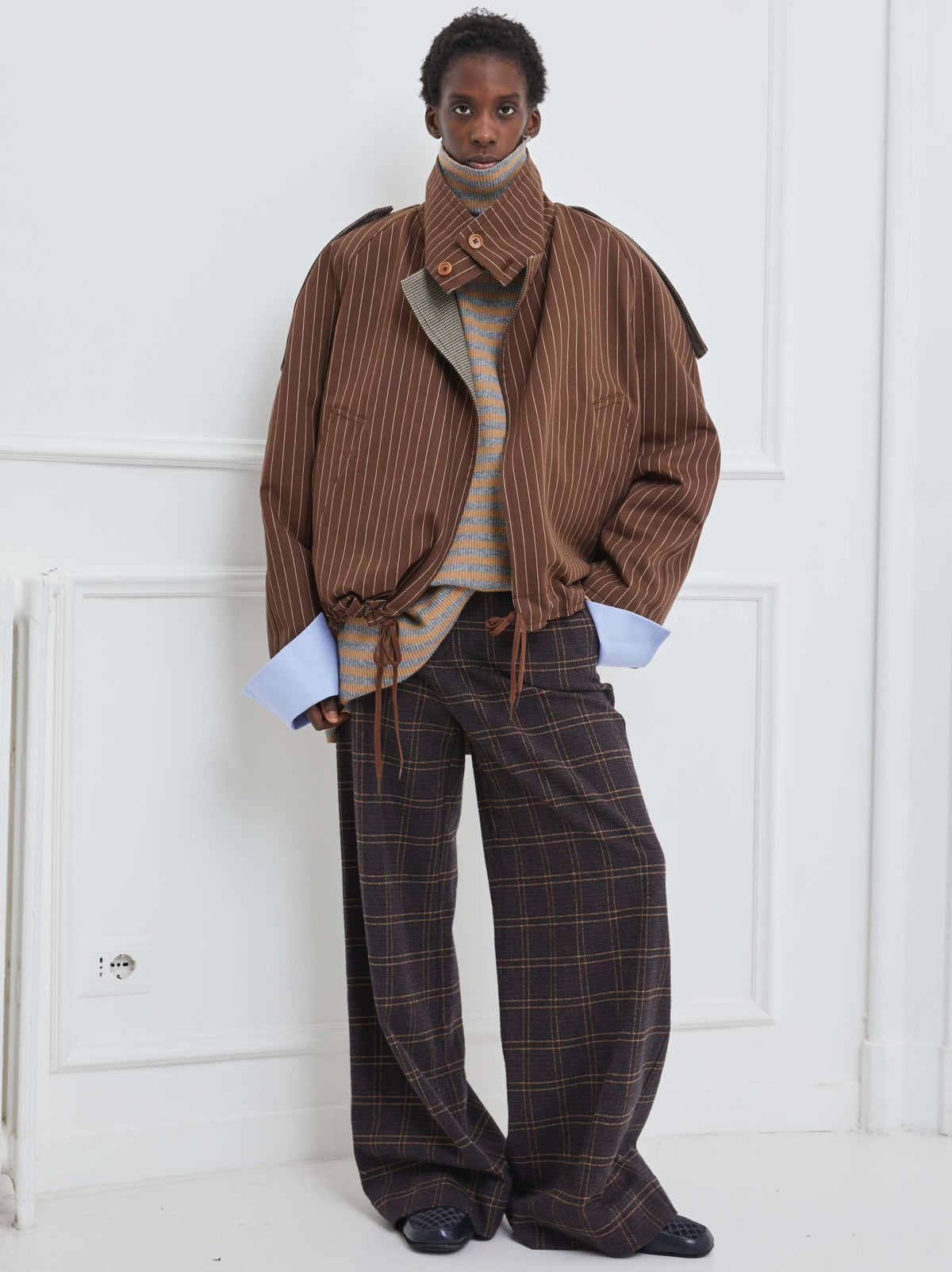 Model is wearing the Brown Pinstripe Bomber Trench by Maison Jejia, part of the House of Woven Stories selection, featuring a relaxed bomber-inspired fit, oversized collar, and adjustable drawstrings.