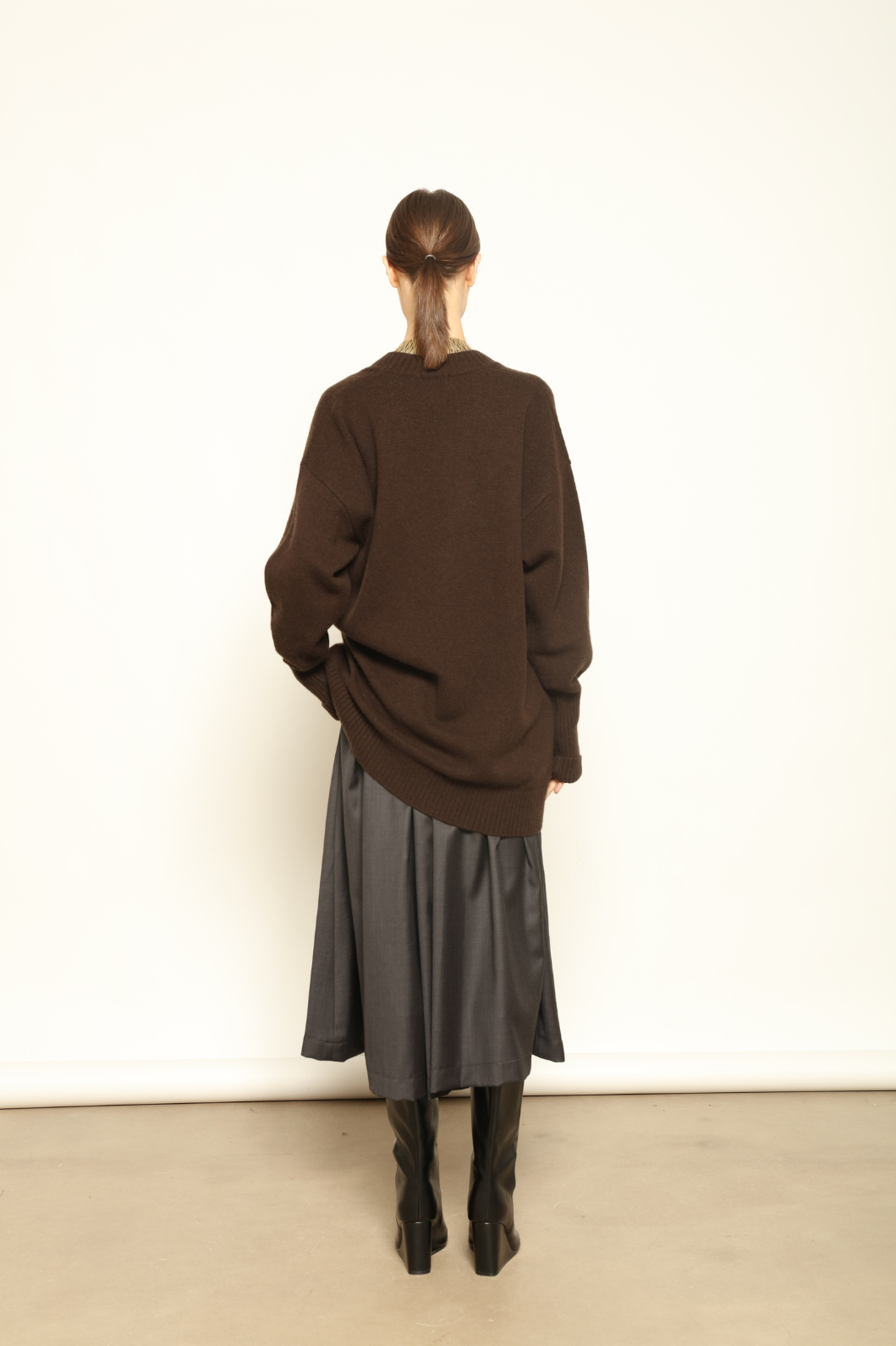 Model is wearing the Chocolate Nina V-Neck Long Sweater by House of Nomad Stories, crafted from 100% pure Inner Mongolia cashmere in a deep chocolate shade, featuring an elongated silhouette, deep V-neckline, soft breathable knit, and timeless sustainable Italian luxury design