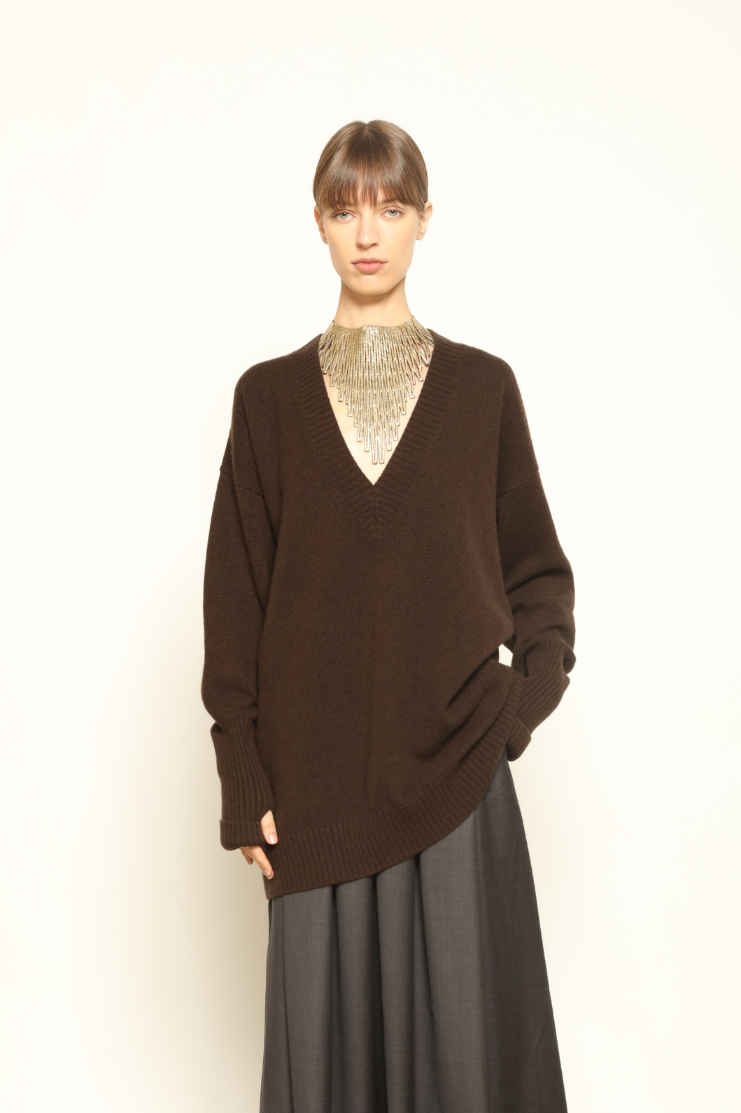 Model is wearing the Chocolate Nina V-Neck Long Sweater by House of Nomad Stories, crafted from 100% pure Inner Mongolia cashmere in a deep chocolate shade, featuring an elongated silhouette, deep V-neckline, soft breathable knit, and timeless sustainable Italian luxury design