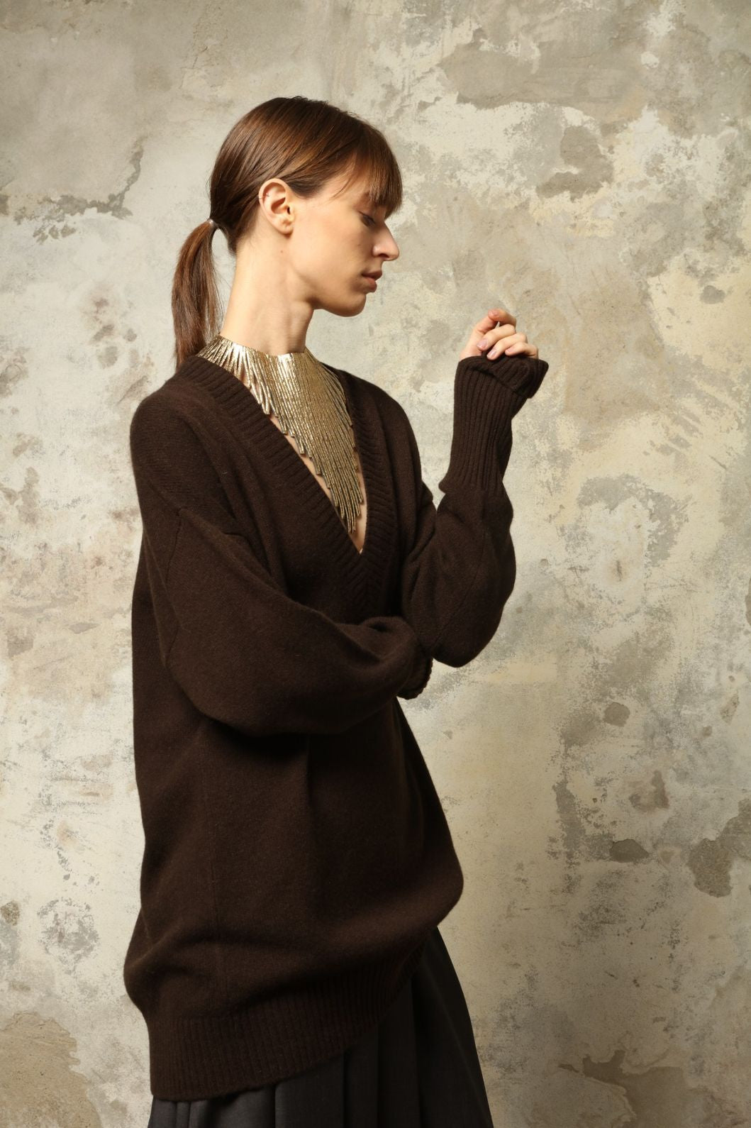 Model is wearing the Chocolate Nina V-Neck Long Sweater by House of Nomad Stories, crafted from 100% pure Inner Mongolia cashmere in a deep chocolate shade, featuring an elongated silhouette, deep V-neckline, soft breathable knit, and timeless sustainable Italian luxury design