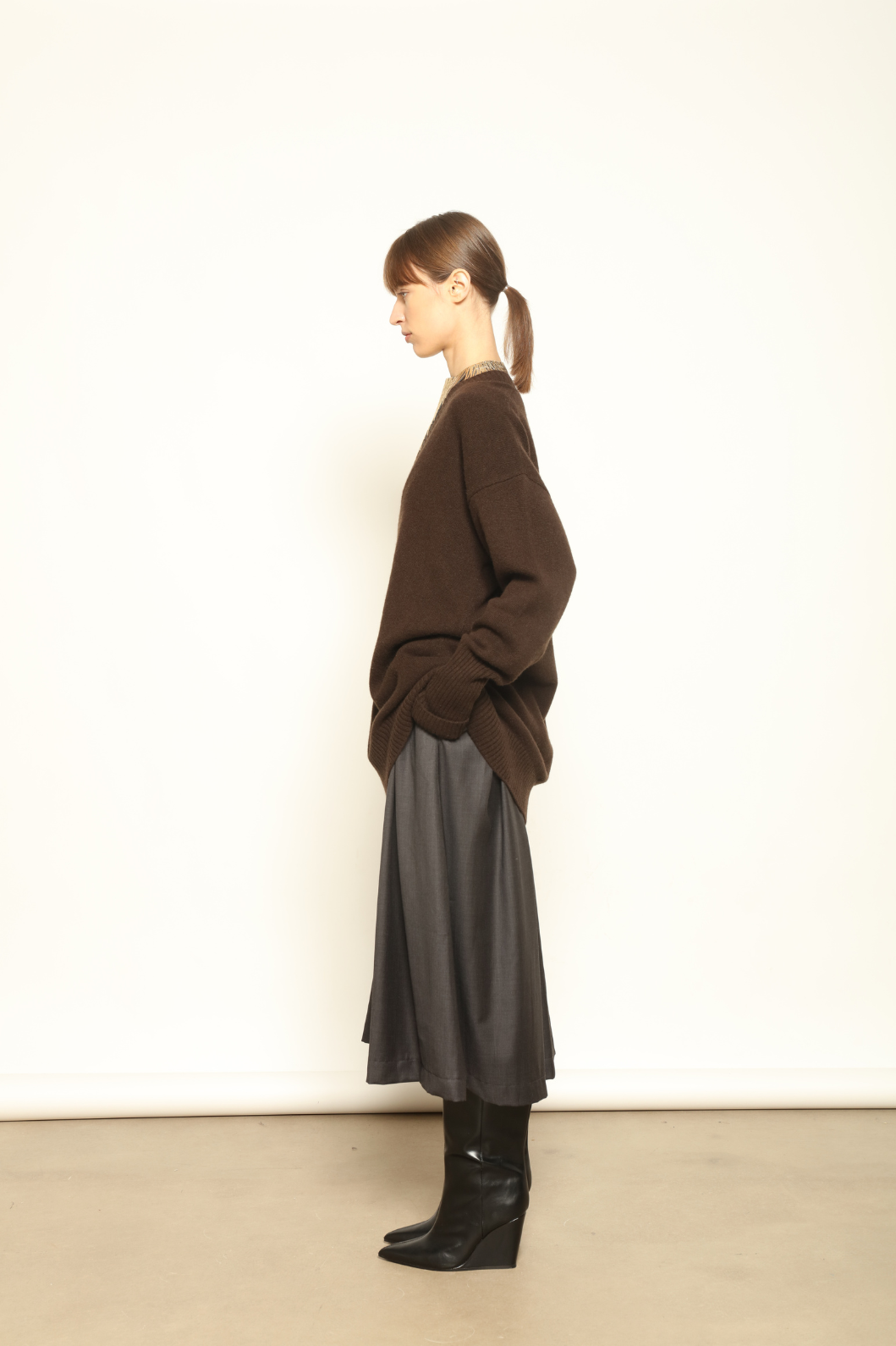 Model is wearing the Chocolate Nina V-Neck Long Sweater by House of Nomad Stories, crafted from 100% pure Inner Mongolia cashmere in a deep chocolate shade, featuring an elongated silhouette, deep V-neckline, soft breathable knit, and timeless sustainable Italian luxury design