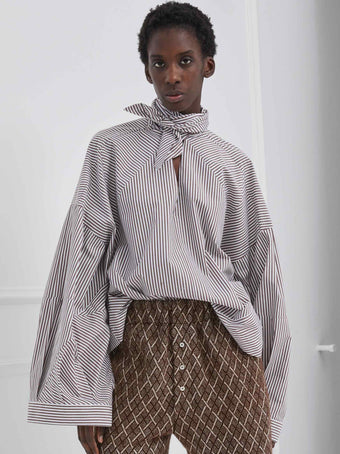 Model is wearing the Clo Brown and White Cotton Stripes Shirt by Maison Jejia, part of the House of Woven Stories selection, featuring puffed sleeves, wrap-style design, and warm brown stripes.