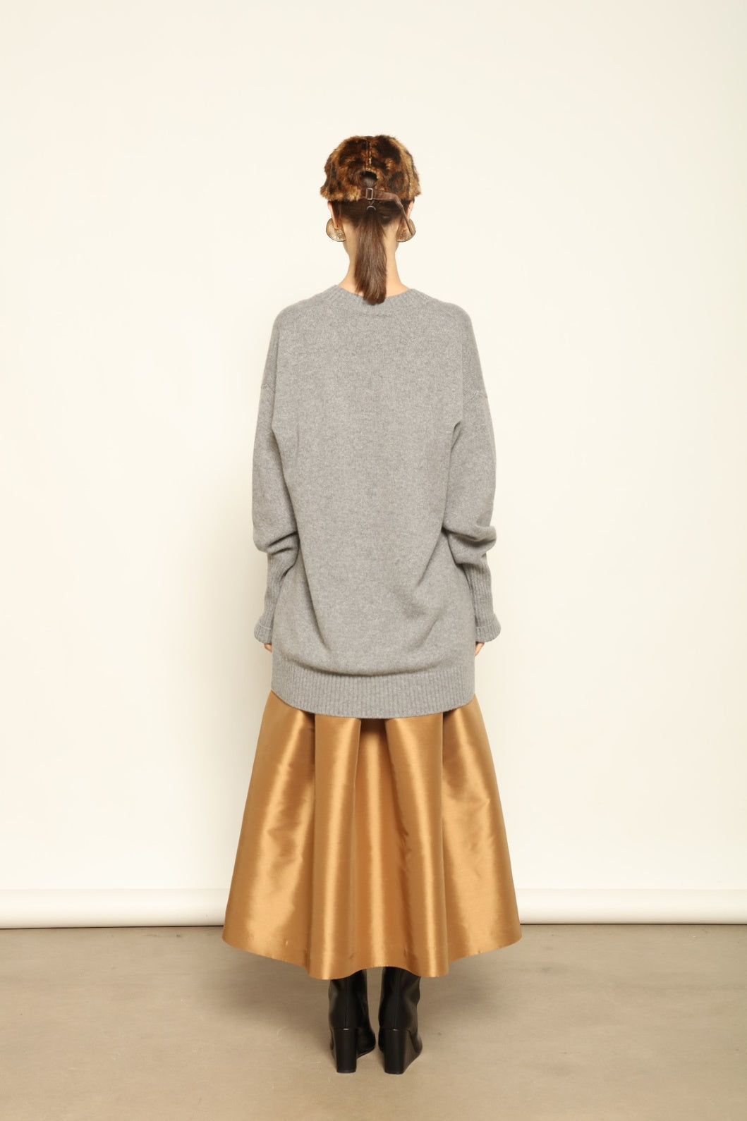 model wearing a gray sweater and gold skirt standing against a white wall.