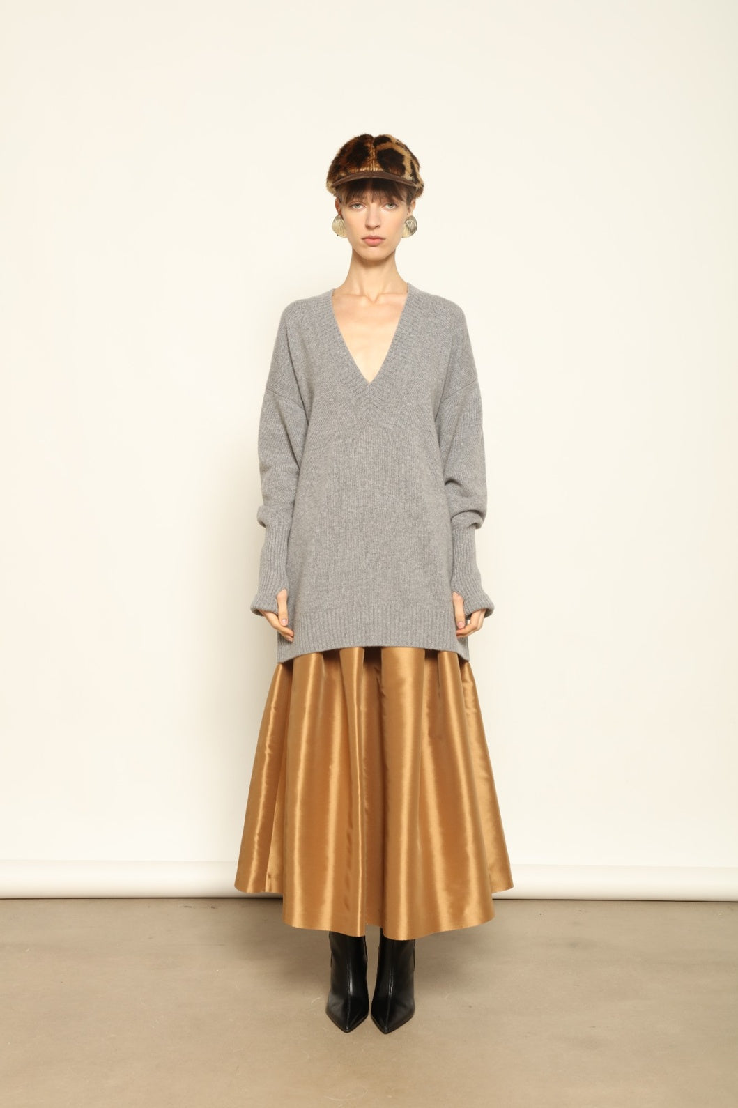 Woman wearing a gray sweater and gold skirt against a white background