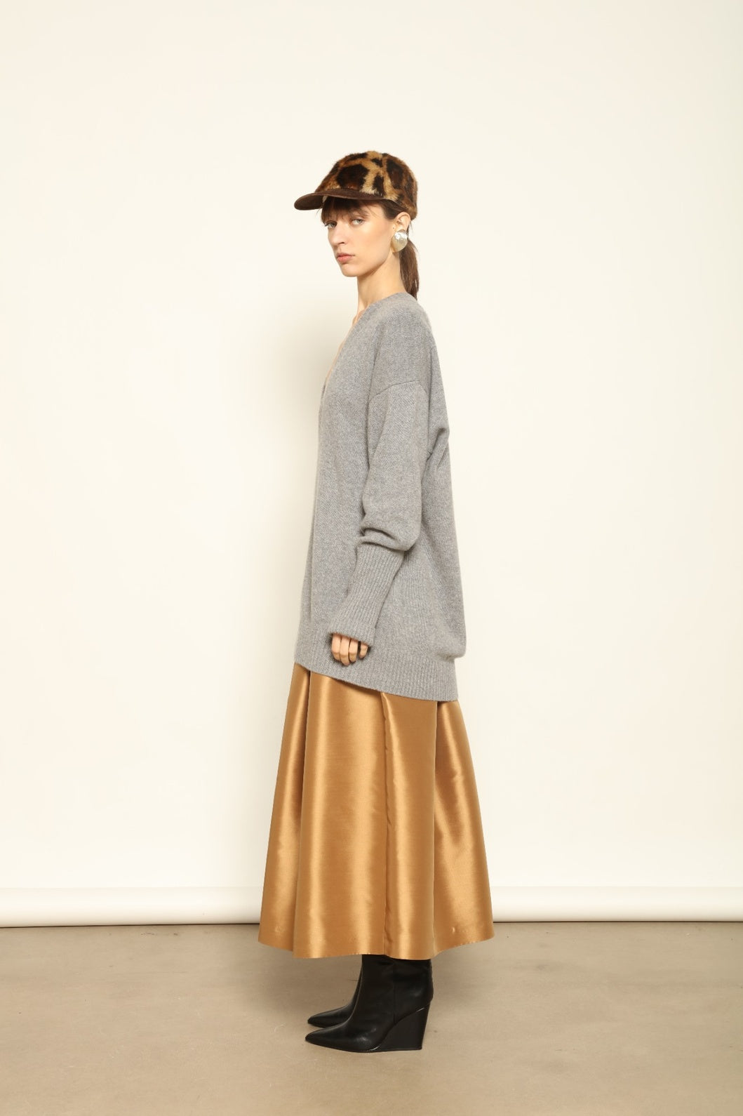 Woman wearing a gray sweater and gold skirt with a white background