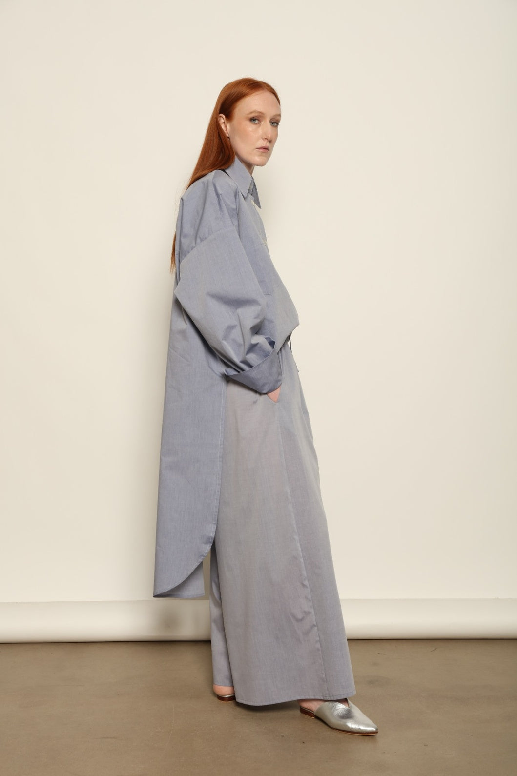 Model is wearing the Dusty Blue Bettina Long Shirt by House of Nomad Stories, crafted from 100% Ratti cotton with an elongated relaxed silhouette, soft dusty blue colour, and refined Italian craftsmanship.