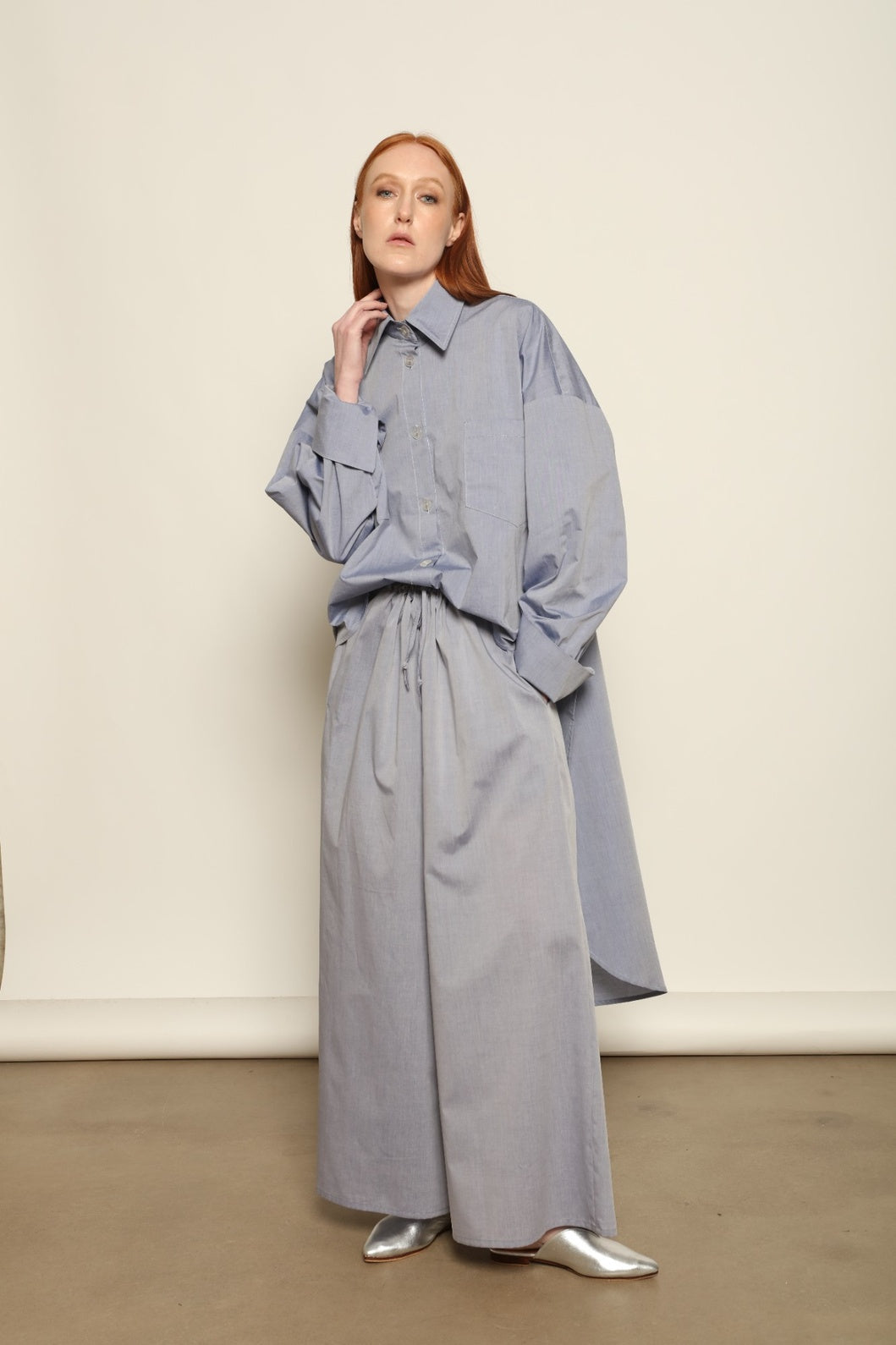 Model is wearing the Dusty Blue Bettina Long Shirt by House of Nomad Stories, crafted from 100% Ratti cotton with an elongated relaxed silhouette, soft dusty blue colour, and refined Italian craftsmanship.