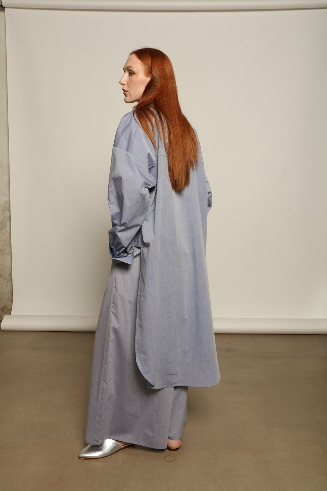 Model is wearing the Dusty Blue Bettina Long Shirt by House of Nomad Stories, crafted from 100% Ratti cotton with an elongated relaxed silhouette, soft dusty blue colour, and refined Italian craftsmanship.