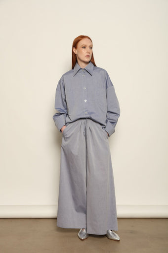 Model is wearing the Dusty Blue Bettina Long Shirt by House of Nomad Stories, crafted from 100% Ratti cotton with an elongated relaxed silhouette, soft dusty blue colour, and refined Italian craftsmanship.