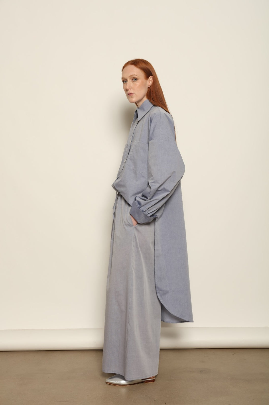Model is wearing the Dusty Blue Bettina Long Shirt by House of Nomad Stories, crafted from 100% Ratti cotton with an elongated relaxed silhouette, soft dusty blue colour, and refined Italian craftsmanship.