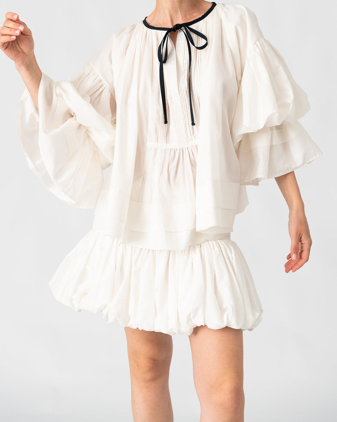 Model is wearing the Favignana Cotton and Silk Blouse by Les Vacances d’Irina, a vintage-inspired handmade blouse with pleated three-quarter sleeves, black bow neckline, and luxurious cotton-silk fabric, available at House of Nomad Stories.