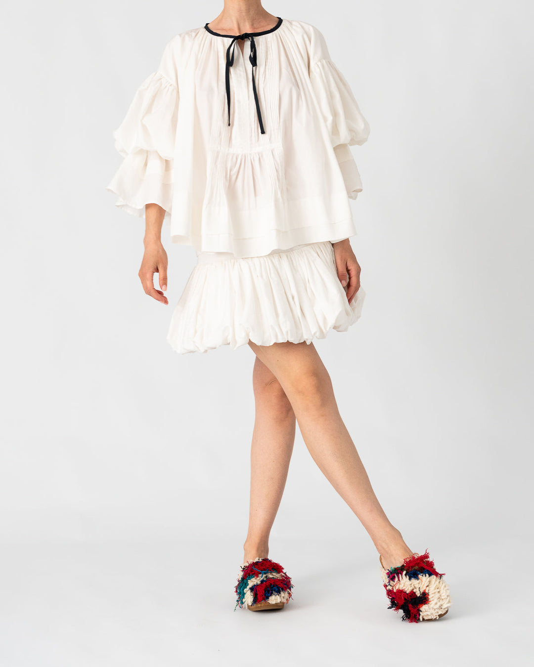 Model is wearing the Favignana Cotton and Silk Blouse by Les Vacances d’Irina, a vintage-inspired handmade blouse with pleated three-quarter sleeves, black bow neckline, and luxurious cotton-silk fabric, available at House of Nomad Stories.