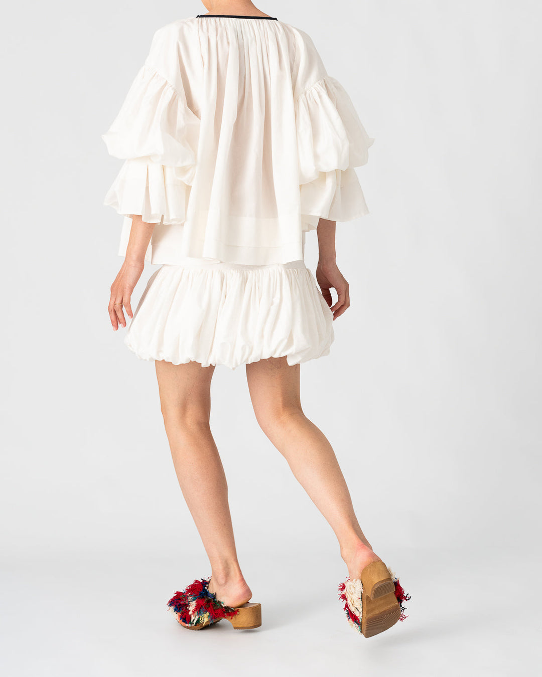 Model is wearing the Favignana Cotton and Silk Blouse by Les Vacances d’Irina, a vintage-inspired handmade blouse with pleated three-quarter sleeves, black bow neckline, and luxurious cotton-silk fabric, available at House of Nomad Stories.