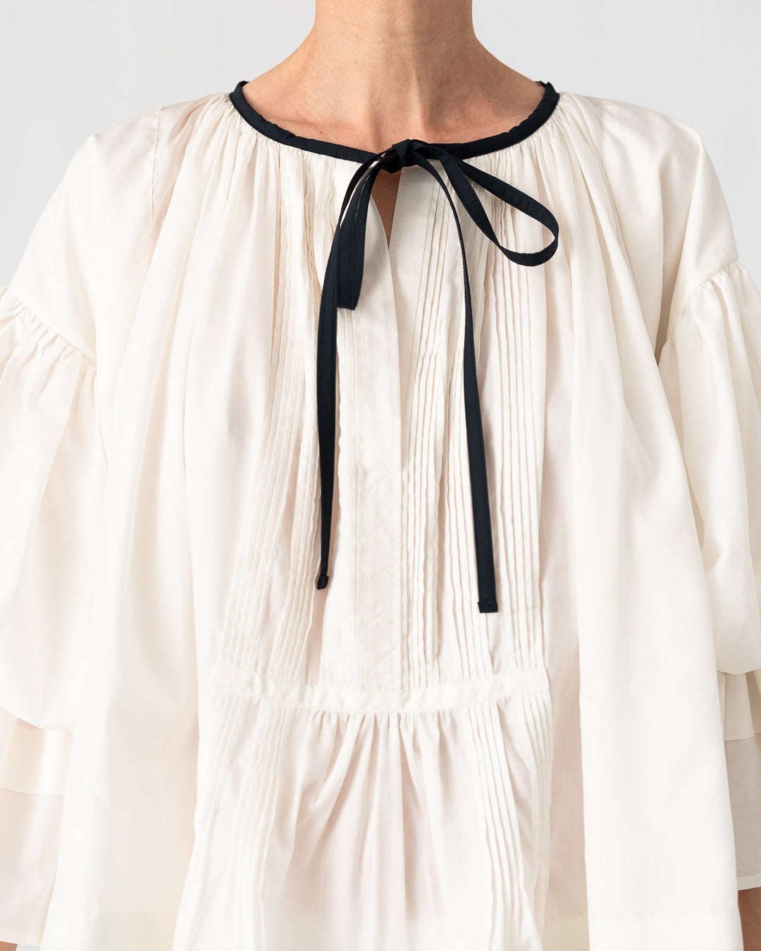 Model is wearing the Favignana Cotton and Silk Blouse by Les Vacances d’Irina, a vintage-inspired handmade blouse with pleated three-quarter sleeves, black bow neckline, and luxurious cotton-silk fabric, available at House of Nomad Stories.