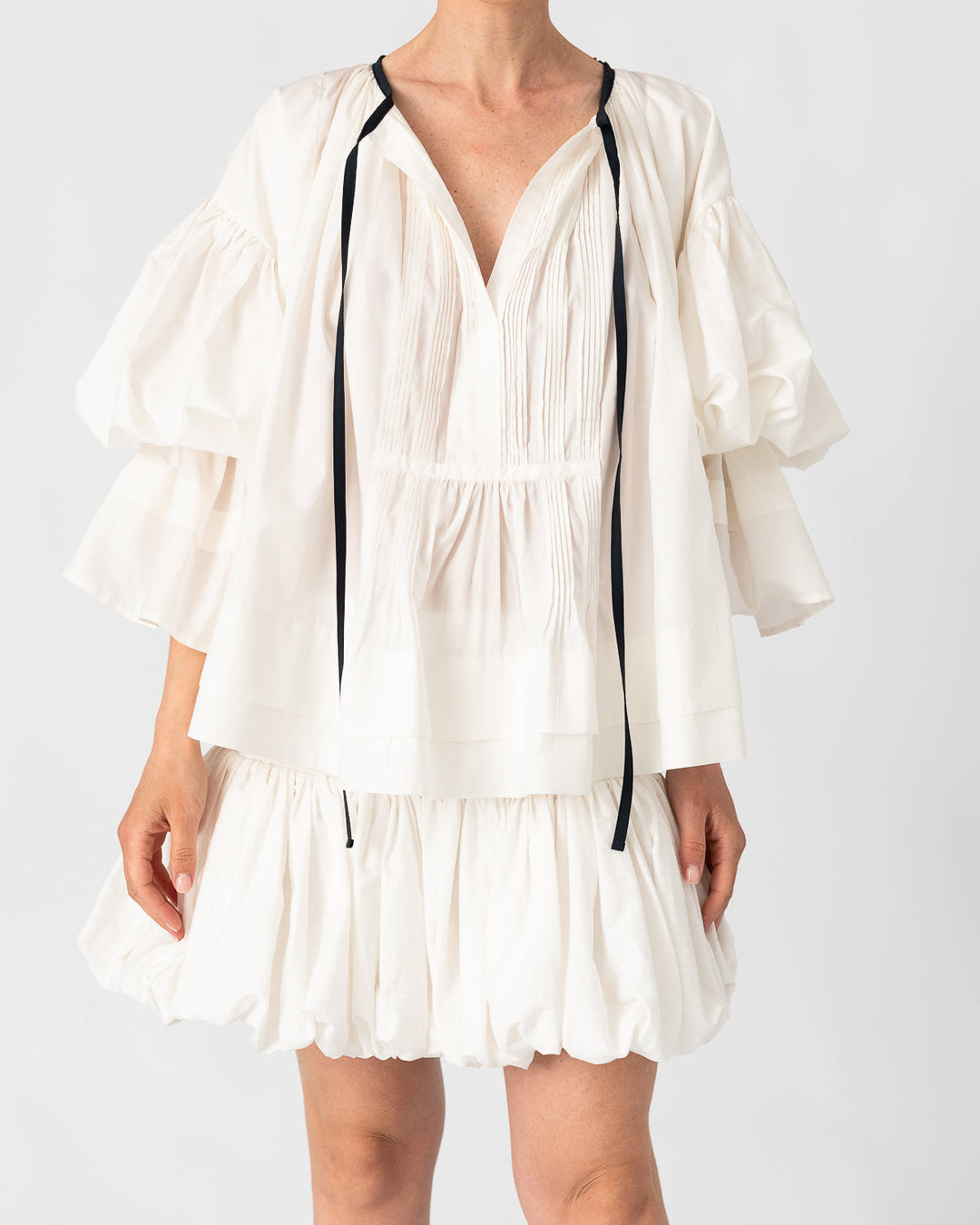 Model is wearing the Favignana Cotton and Silk Blouse by Les Vacances d’Irina, a vintage-inspired handmade blouse with pleated three-quarter sleeves, black bow neckline, and luxurious cotton-silk fabric, available at House of Nomad Stories.