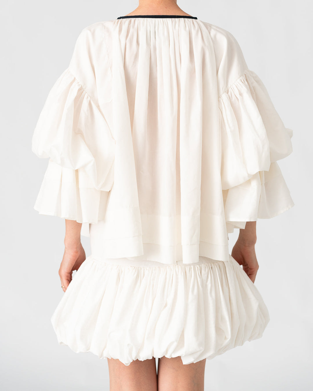 Model is wearing the Favignana Cotton and Silk Blouse by Les Vacances d’Irina, a vintage-inspired handmade blouse with pleated three-quarter sleeves, black bow neckline, and luxurious cotton-silk fabric, available at House of Nomad Stories.